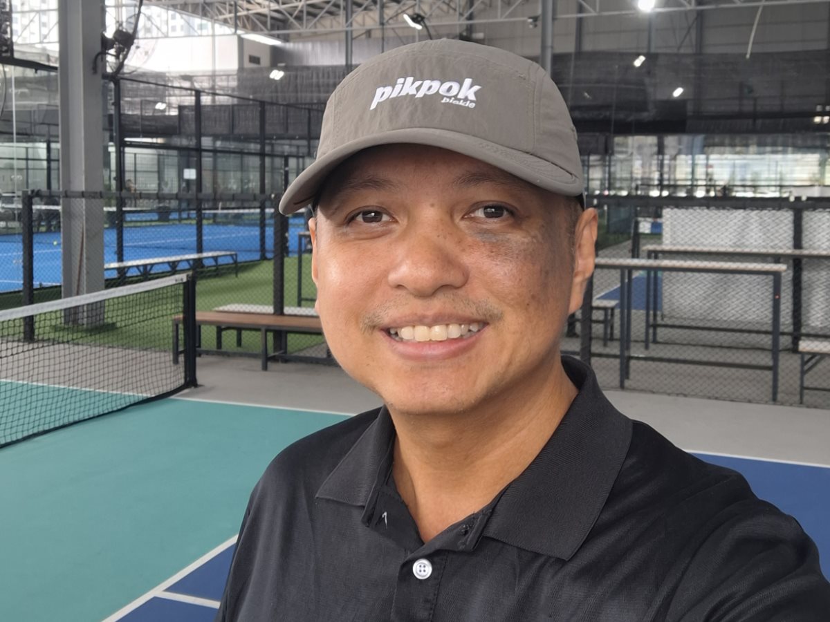 Your coach, smiling on an indoor pickleball court with the courts and netting behind him